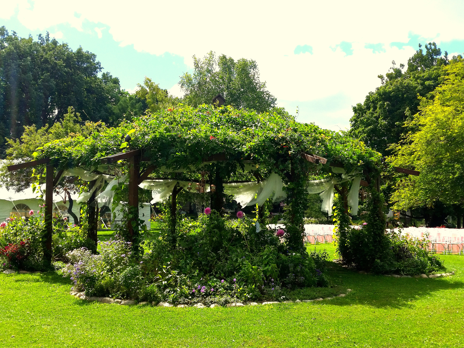 Looking at the Reception tent and the Ceremony chairs through the Flowering Gazebo
